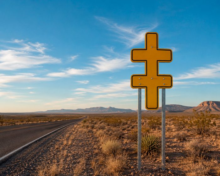 Yellow sign in the form of a double dagger, mounted on two posts beside a desert highway