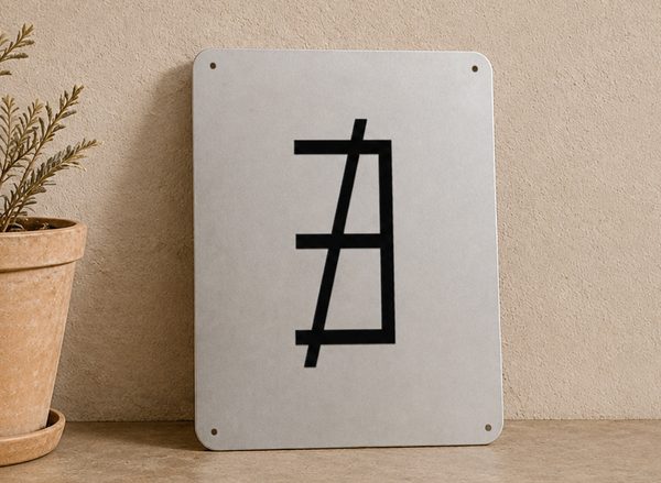 Powder-coated aluminum sign carrying a black constructed glyph, propped against a wall beside a potted plant